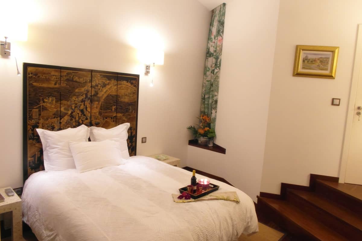 Habitación de hotel con una cama grande, una mesita de noche, una botella de champán y una bandeja con vela y flores.