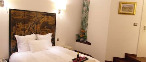 Habitación de hotel con una cama grande, una mesita de noche, una botella de champán y una bandeja con vela y flores.