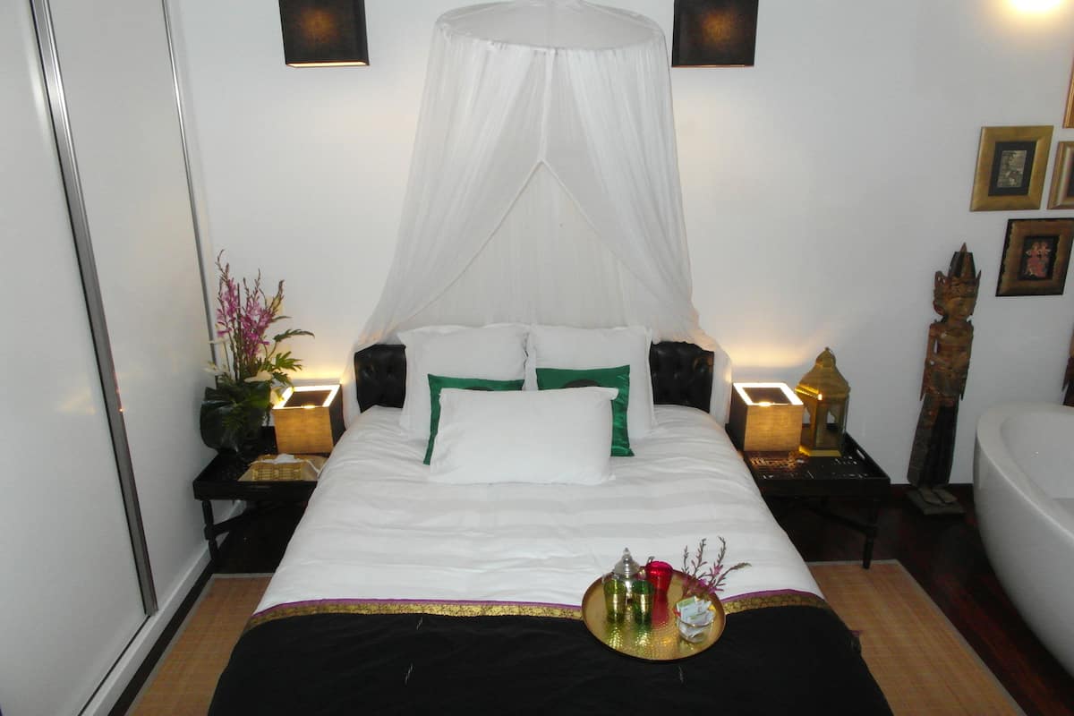 Un dormitorio con cama, mesita de noche, lámpara de noche, luz empotrada en la pared, adorno decorativo y cuadro colgado en la pared.