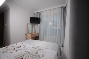 A hotel room with a bed, a TV mounted on the wall, a wooden bedside table, and a window with curtains.