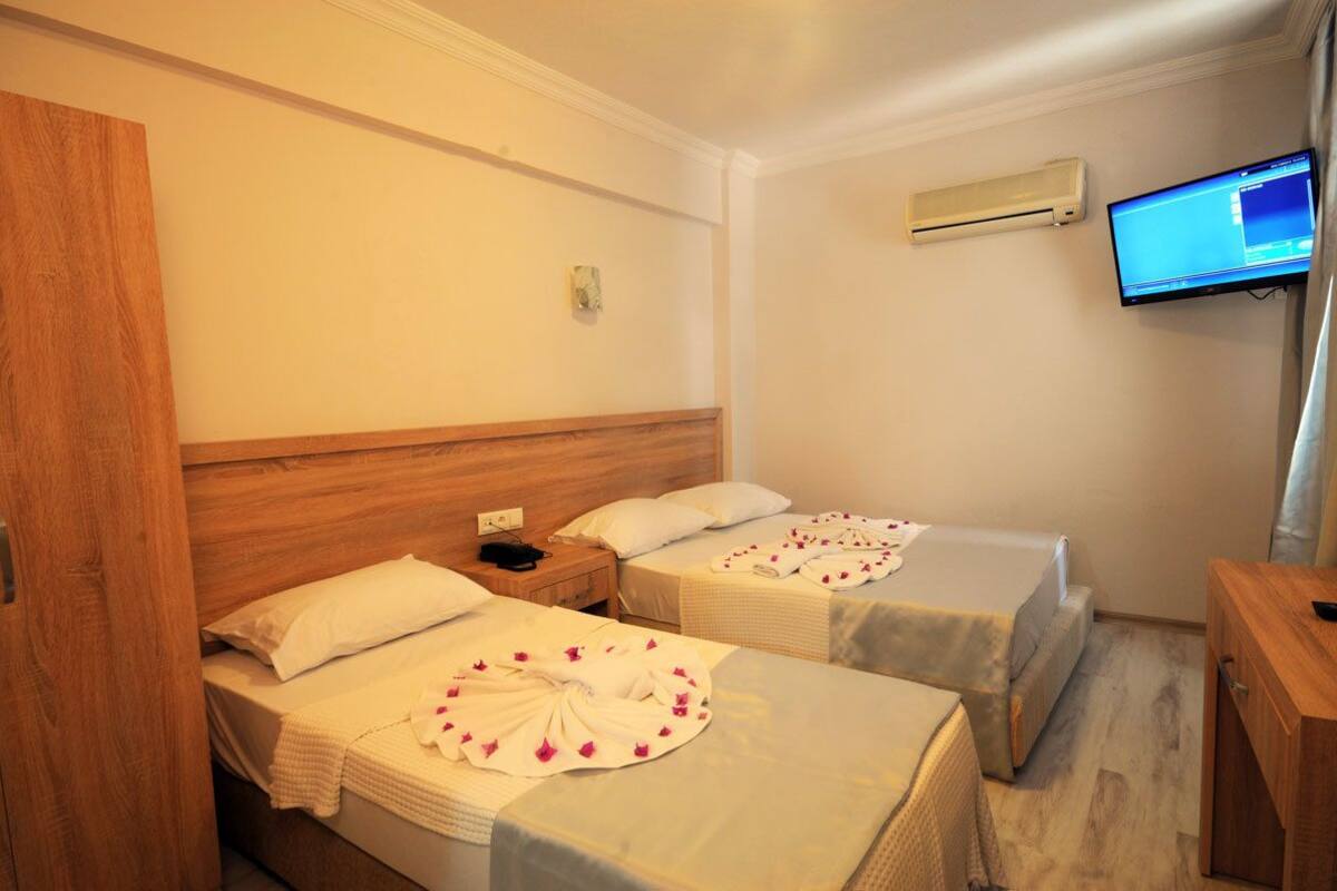 A hotel room with two beds, a wooden headboard, a TV mounted on the wall, and an air conditioning unit.