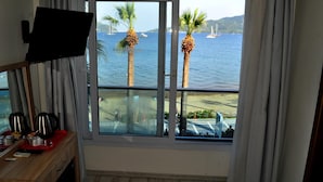Habitación con un amplio ventanal con vistas a una playa y al mar, con un escritorio y un televisor en el lado izquierdo.