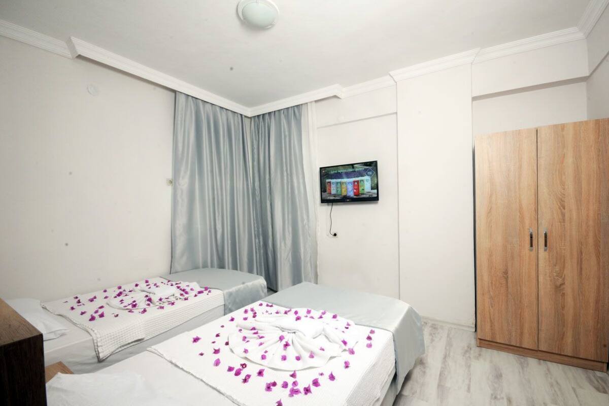 A hotel room with two beds, a wooden wardrobe, a television on the wall, and a window with curtains.