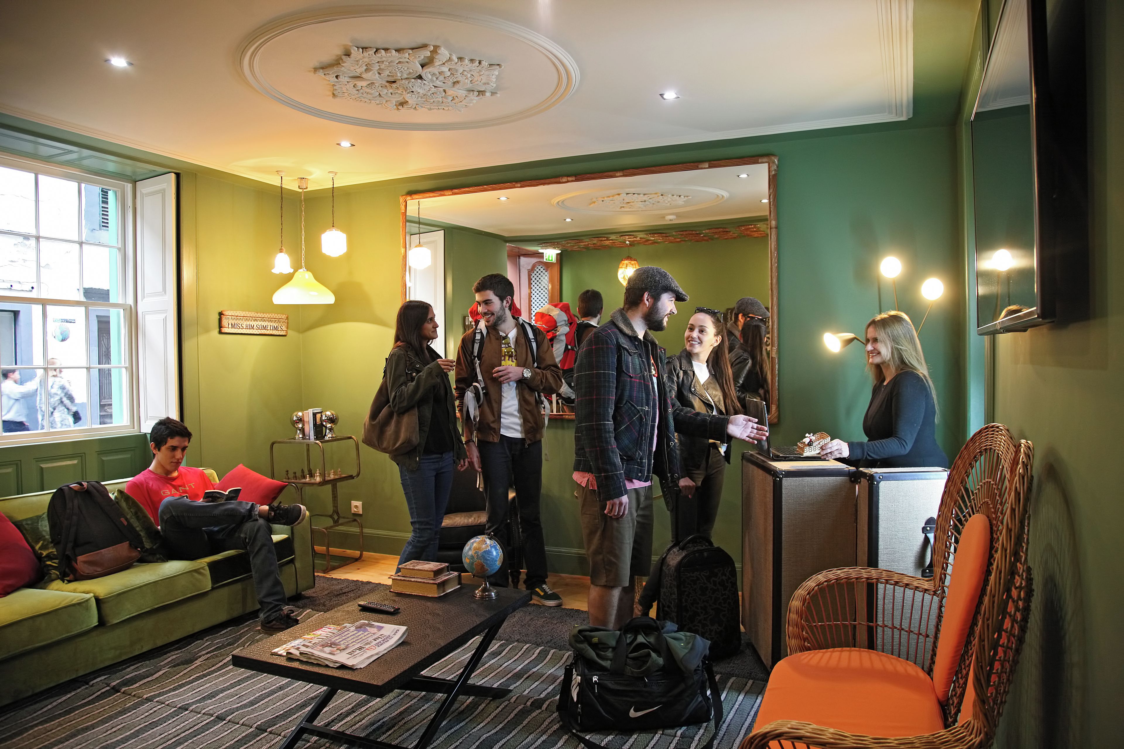 A lobby with a green wall, a reception desk, a wicker chair, and a sofa with a person sitting on it.