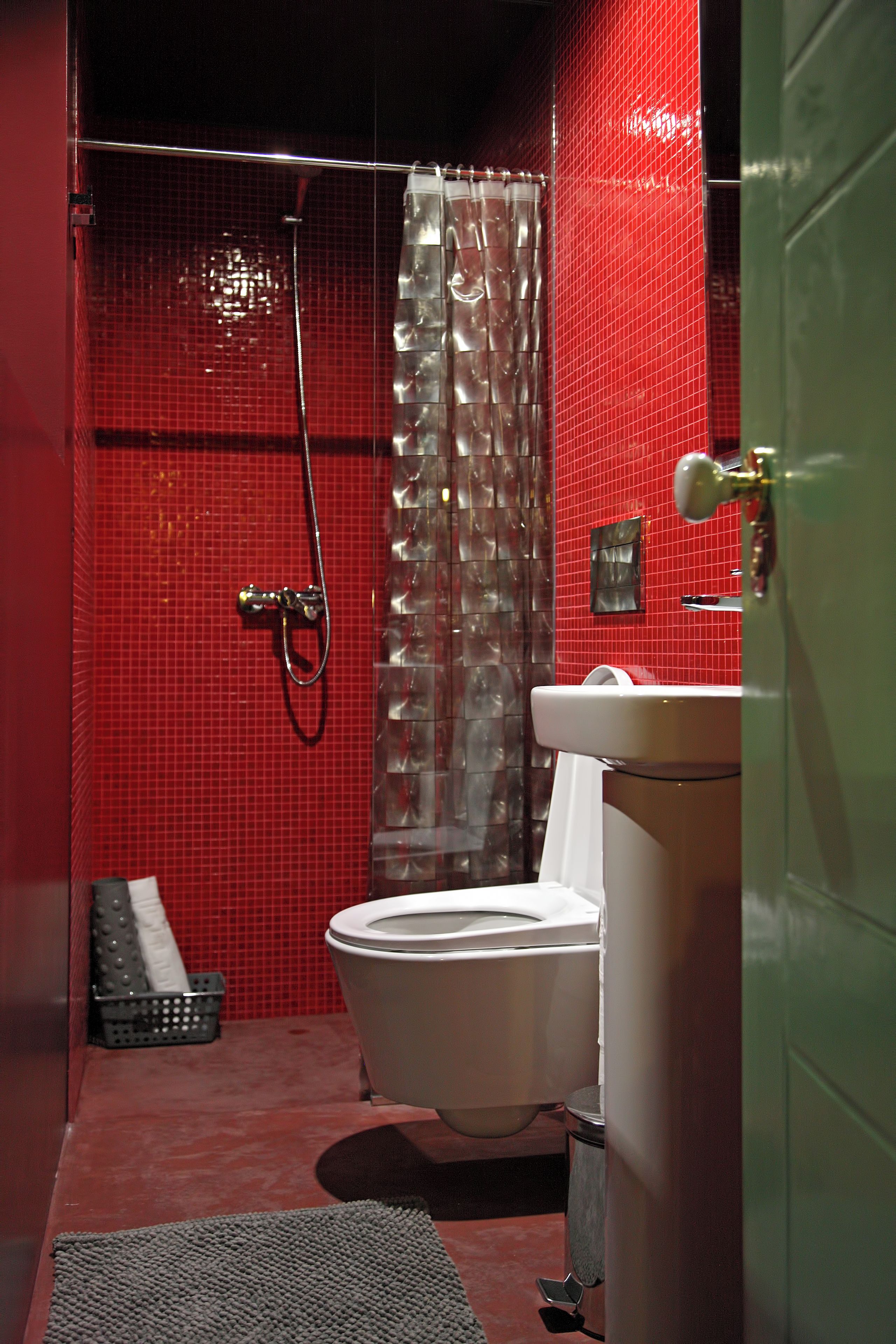 A bathroom with a red tiled wall, a shower with a glass door, a white toilet, and a sink with a mirror.