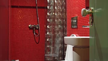 A bathroom with a red tiled wall, a shower with a glass door, a white toilet, and a sink with a mirror.