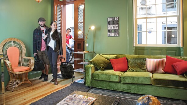 A cozy room with a green sofa, wicker chair, and a sign that reads "TIME TO DRINK CHAMPAGNE AND DANCE ON THE TABLE." - 29 Madeira Hostel (Funchal)