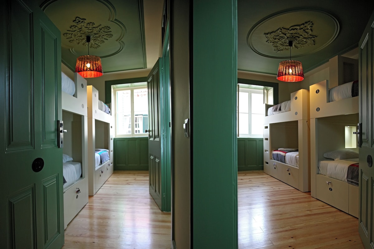 Quarto com beliches, piso de madeira e porta verde.