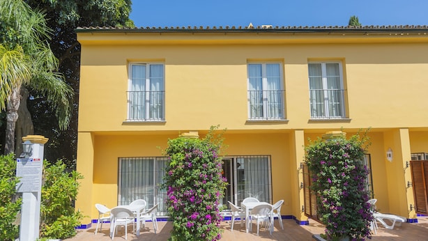 A yellow building with three windows, white chairs, and two potted plants with purple flowers. - Apartamentos Soho Boutique Vistahermosa  (El Puerto de Santa Maria)