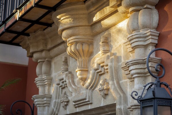 Detalle arquitectónico de piedra con columnas labradas y barandilla de balcón de metal.