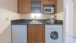 A compact kitchen with wooden cabinets, a microwave, a dishwasher, and a washing machine. - Apartamentos Soho Boutique Vistahermosa  (El Puerto de Santa Maria)