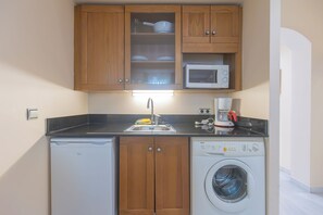 Una cocina compacta con armarios de madera, un microondas, un lavavajillas y una lavadora.