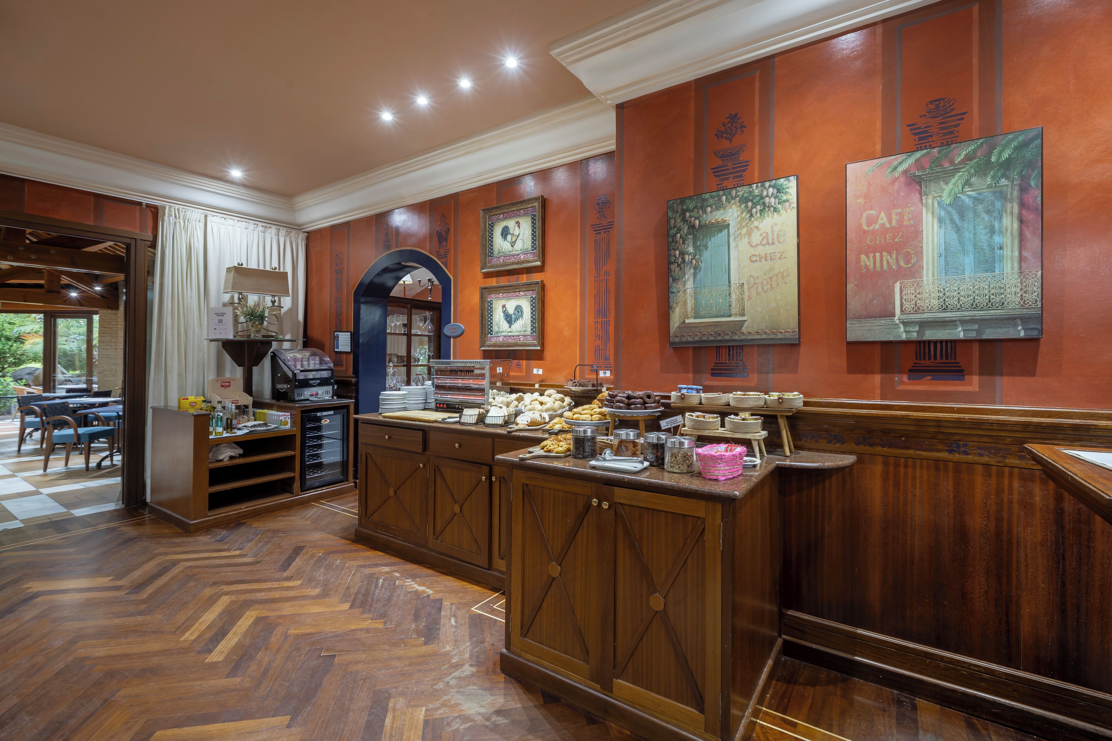 Un vestíbulo de hotel con mostrador de recepción, una estación de café y un área de comedor con un patrón de suelo en espiga.