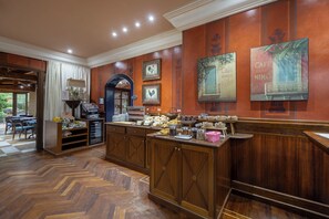 Eine Hotelhalle mit einer Rezeption, einer Kaffeestation und einem Essbereich mit Fischgrätparkett.