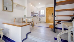 A kitchen with a washing machine, a dining area with a table and chairs, and a staircase with a wooden railing. - Apartamentos Soho Boutique Vistahermosa  (El Puerto de Santa Maria)