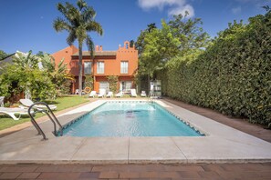 A swimming pool with lounge chairs, a palm tree, and a building with a tiled roof. - Apartamentos Soho Boutique Vistahermosa  (El Puerto de Santa Maria)