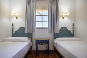 Ein Zimmer mit zwei Betten, einem kleinen Tisch und einem Fenster mit Vorhängen.