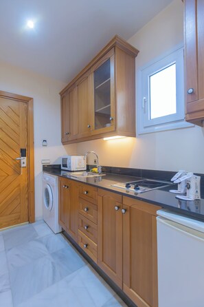 Cocina compacta con armarios de madera, microondas integrado, lavadora y una ventana sobre el fregadero.