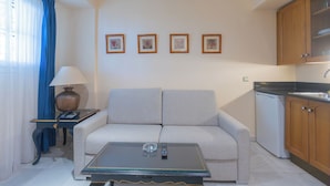 A living room with a sofa, a coffee table, a lamp, and a kitchen area with cabinets and a refrigerator. - Apartamentos Soho Boutique Vistahermosa  (El Puerto de Santa Maria)