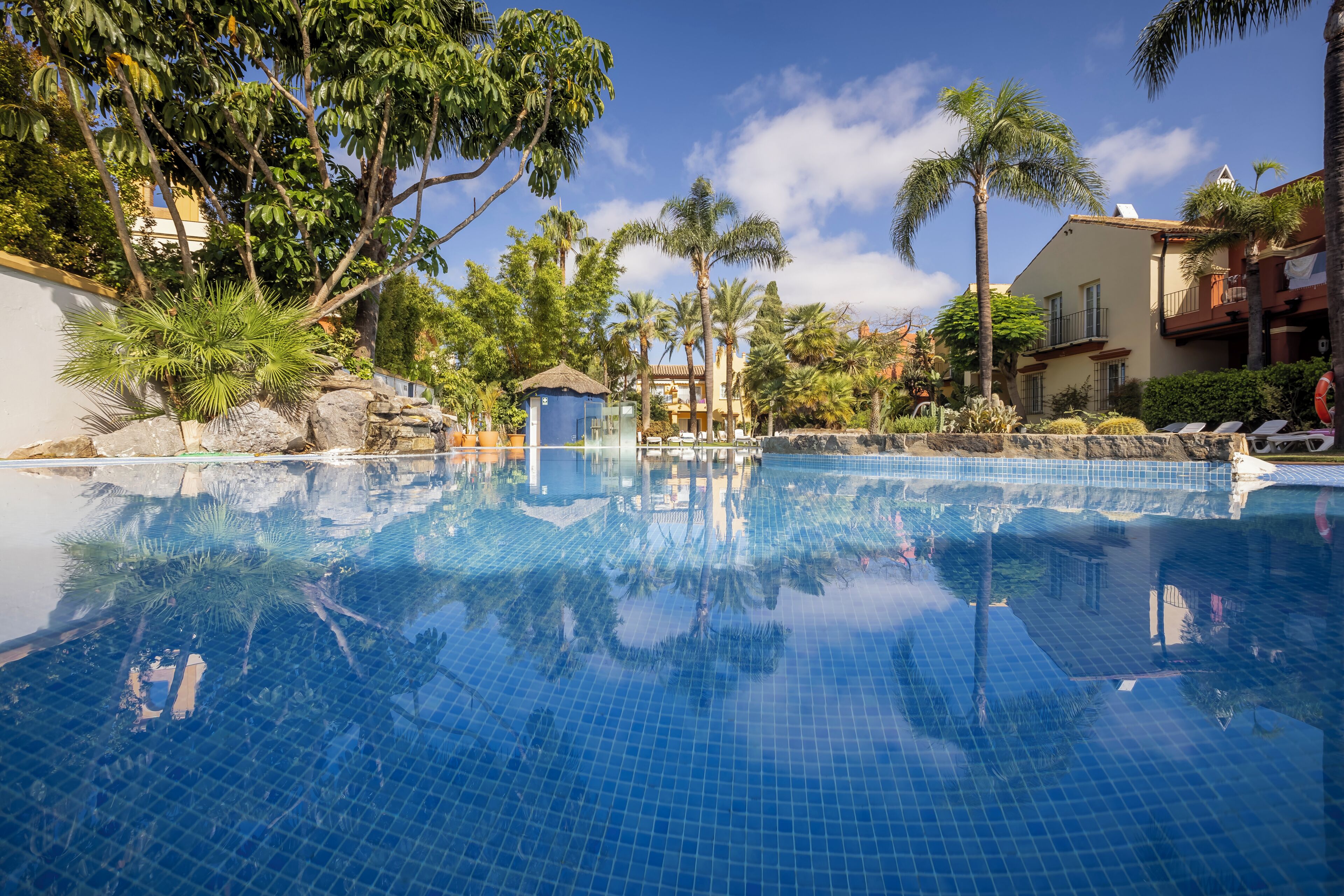 Una piscina azul cristalina rodeada de vegetación tropical y una pequeña cabaña.