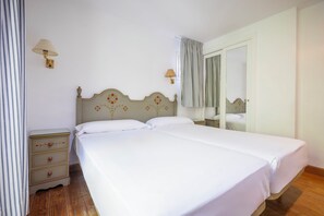 Una cama doble con cabecera de madera, una mesita de noche con cajones, una lámpara de pared y una ventana con cortinas a rayas.