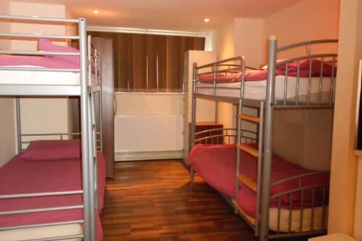 A room with bunk beds, wooden flooring, and a window with blinds.
