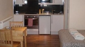 A compact kitchen with a microwave, oven, and sink. There is a wooden dining table and chairs, and a patterned sofa. - 247 London Studios (London)