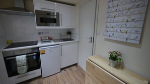 A compact kitchen with white cabinets, a stainless steel oven, a dishwasher, and a wooden bench with a potted plant. - 247 London Studios (London)