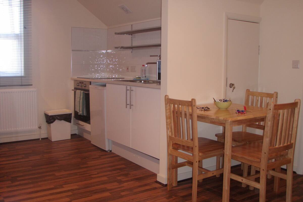 A compact kitchen with white cabinets, a wooden dining table, and chairs.