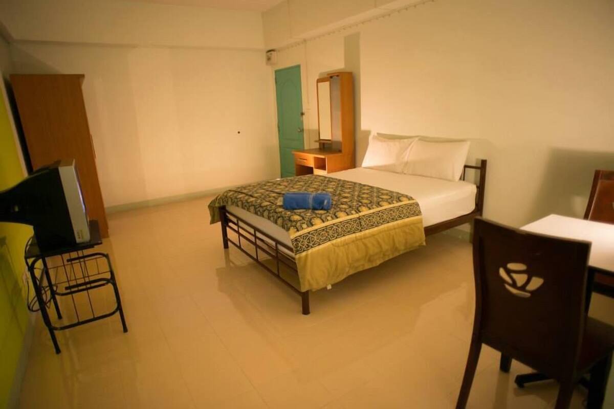 A bedroom with a bed, a bedside table, a mirror, a chair, and a television.