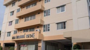 Un hôtel à plusieurs étages, doté d’une façade beige, de nombreux balcons et d’une entrée au niveau du sol agrémentée de plantes en pot.