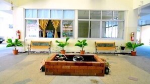Un espace d’attente comprenant deux bancs, un jardinier en briques avec des plantes et une grande fenêtre avec des rideaux.