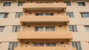 Un immeuble à plusieurs étages, avec une enseigne en langue étrangère, des plantes en pot devant l’entrée et un ciel dégagé.