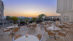 A rooftop terrace with round tables and wicker chairs, overlooking a cityscape at sunset. - Lake River Side Hotel Spa - Ultra All Inclusive (Manavgat)