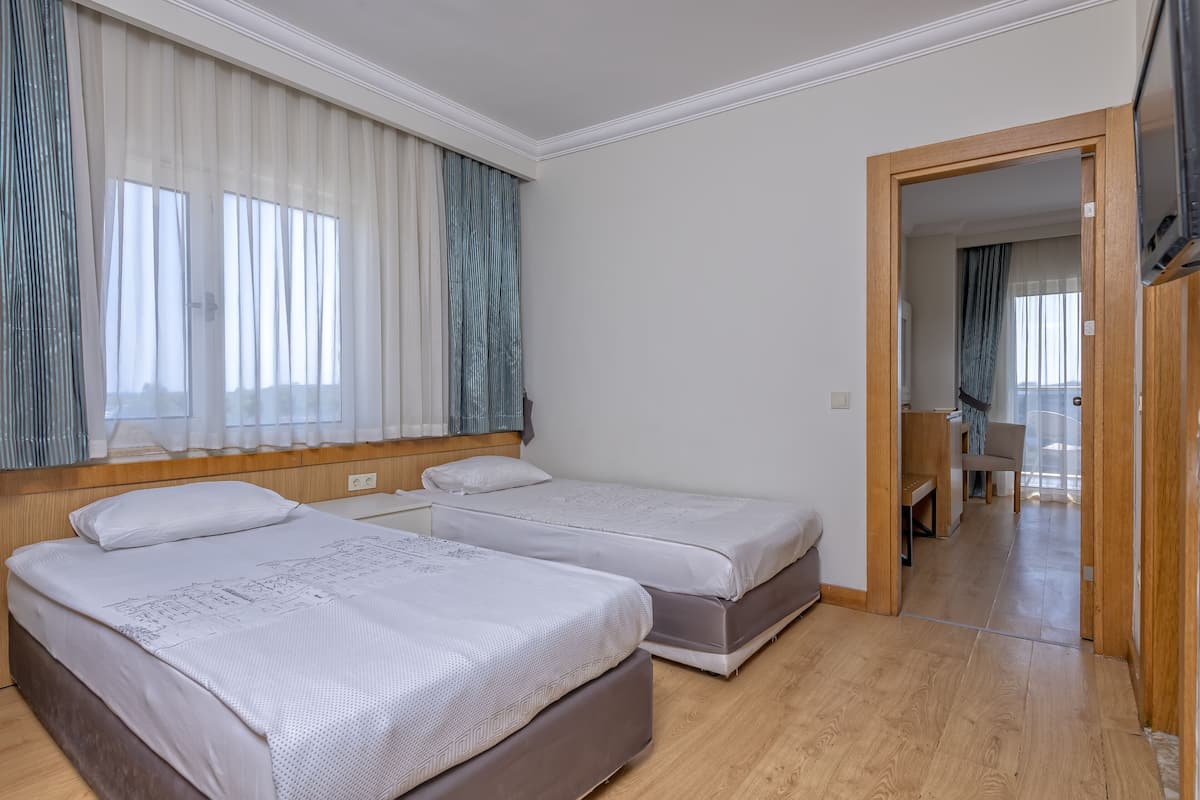 A hotel room with two beds, a wooden floor, and a view of the hallway.