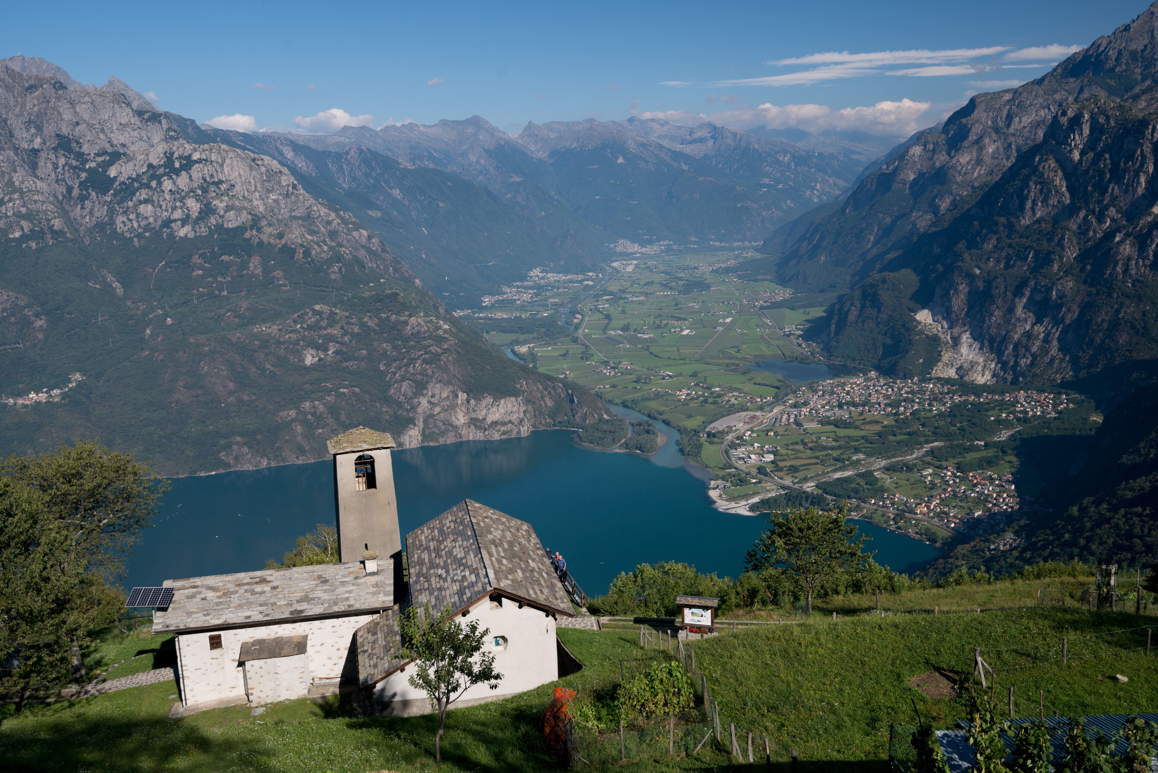 Un paisaje montañoso con un lago, un pequeño edificio con un campanario y un pueblo en el valle.