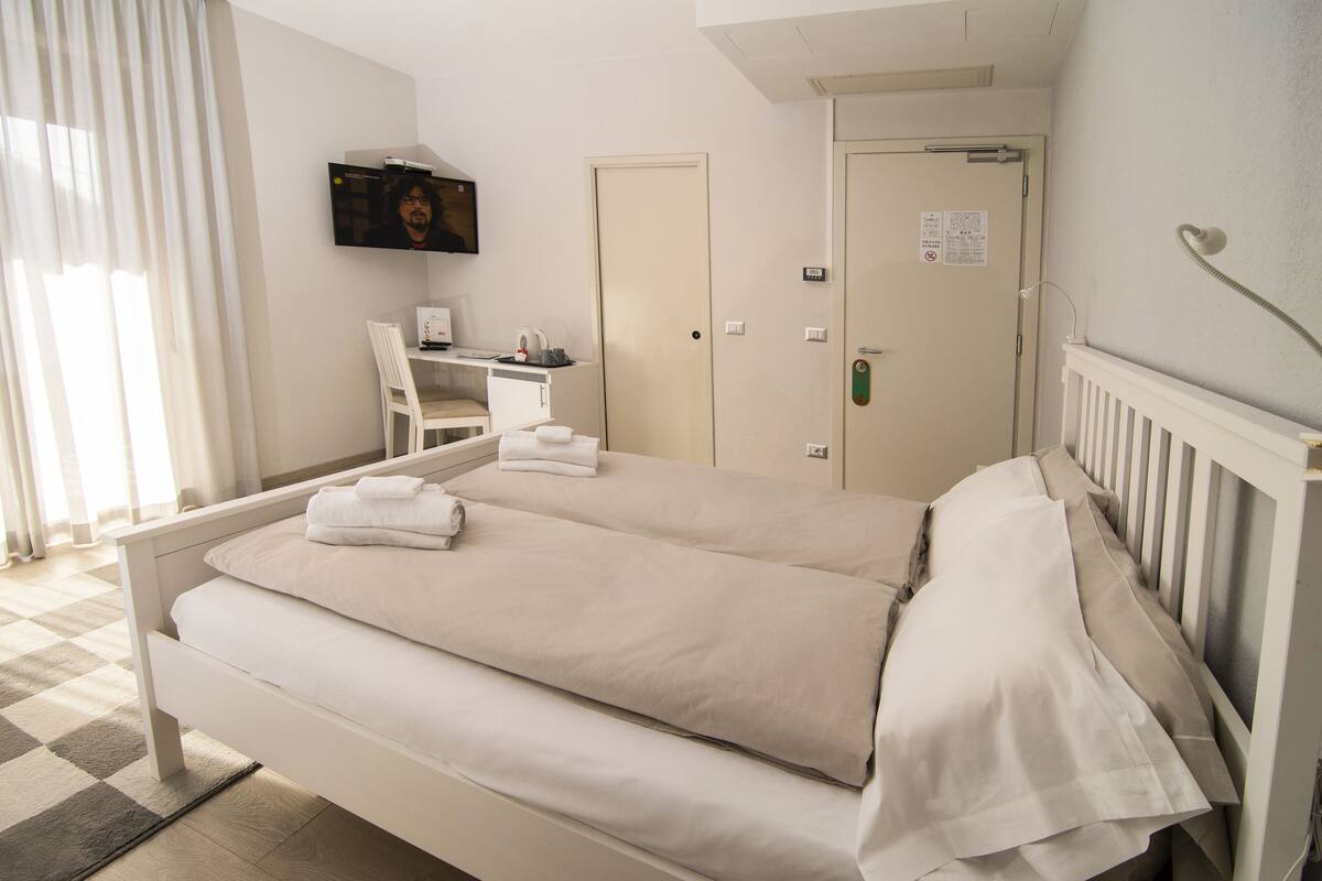 A hotel room with a bed, a desk with a computer, a chair, and a TV on the wall.