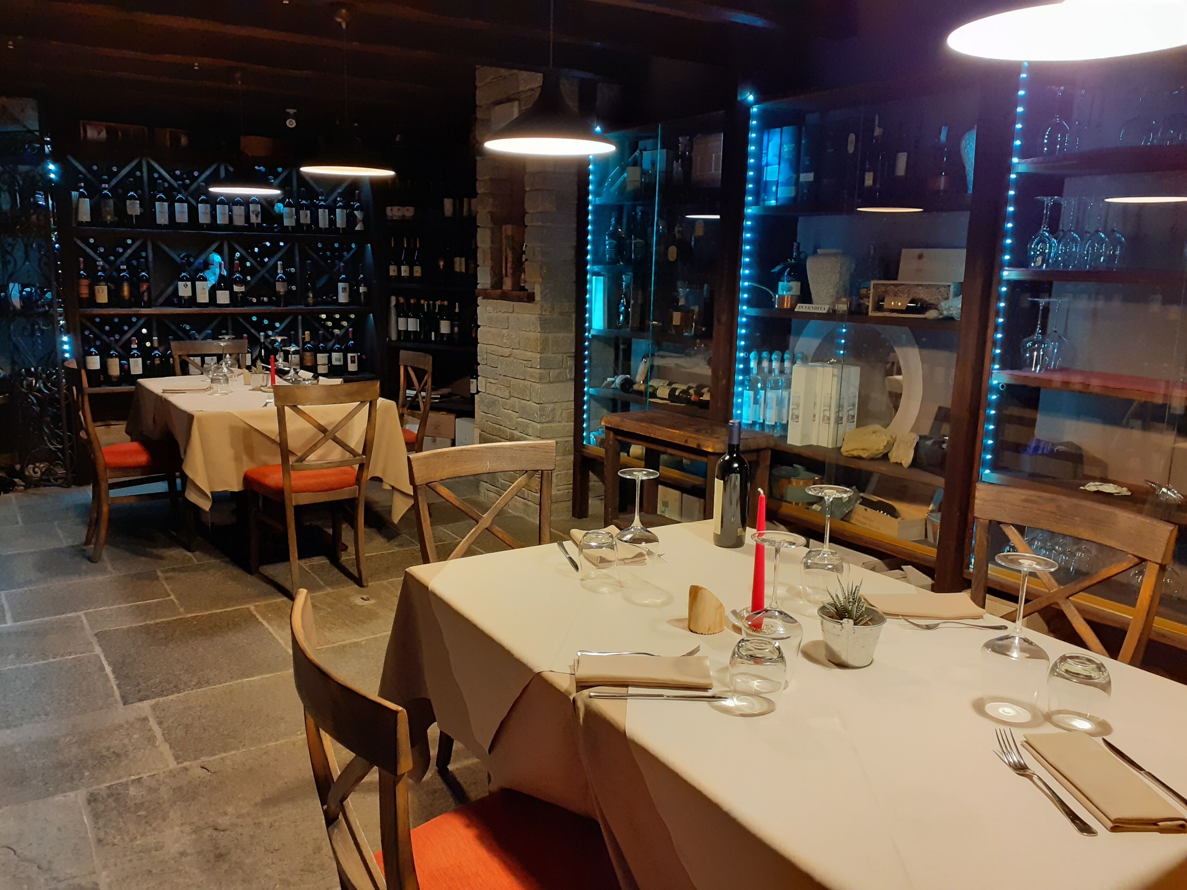 Un ristorante con tavoli apparecchiati, bottiglie di vino sugli scaffali e una parete in pietra.