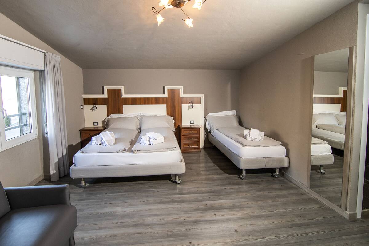 A bedroom with two beds, a wooden floor, a large mirror, and a window with curtains.