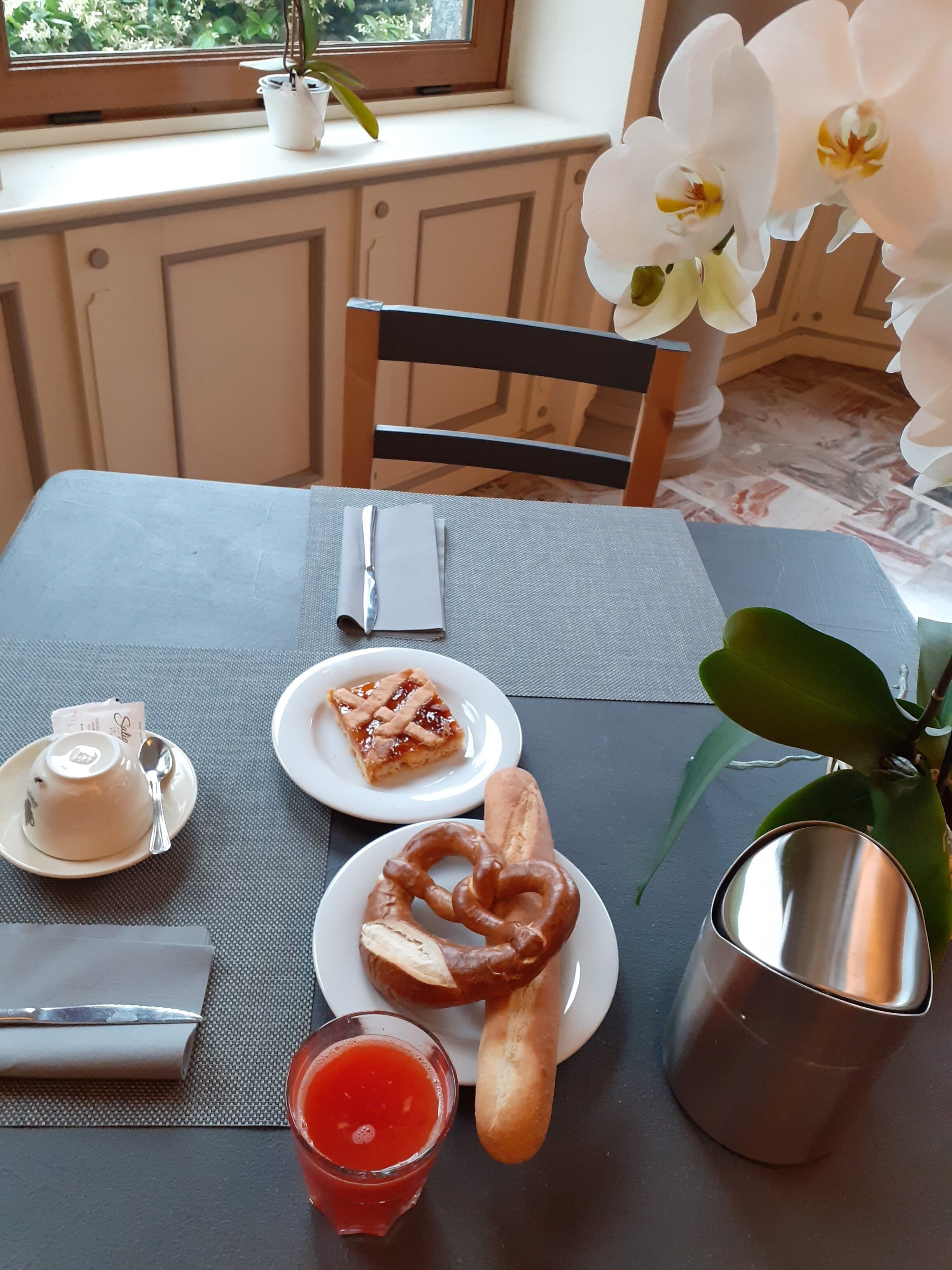 A table set with a plate of food, a glass of red drink, a metal cup, and a napkin.