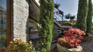 Un bâtiment en pierre doté d’une entrée en verre, d’un escalier en pierre et d’un jardin agrémenté d’arbustes et de fleurs.