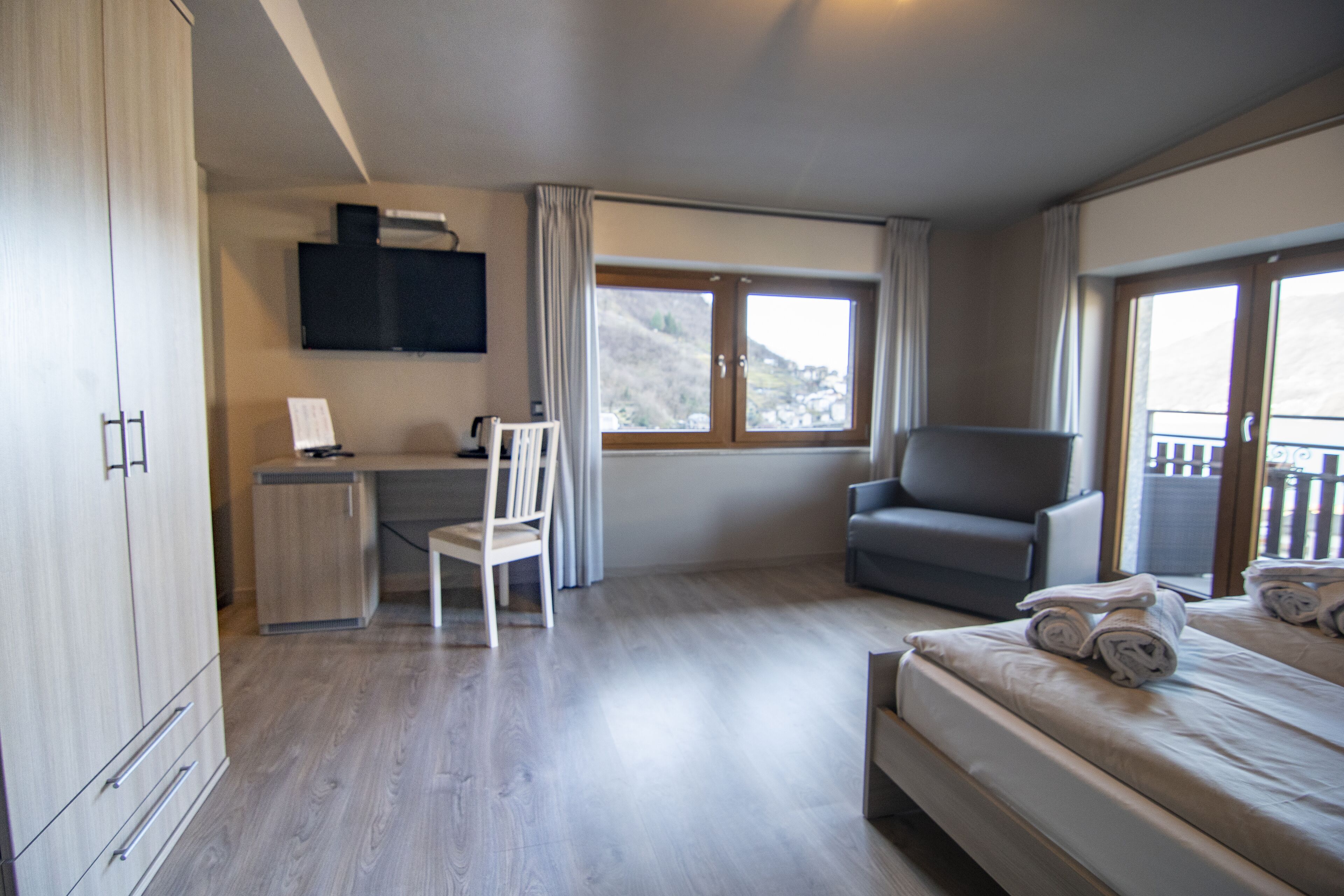 A hotel room with a bed, a desk, a chair, a TV, and a balcony.