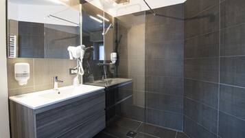 Een moderne badkamer met een grote spiegel, een witte wastafel, een donkerd badmeubel en een douchegedeelte met donkere tegels.