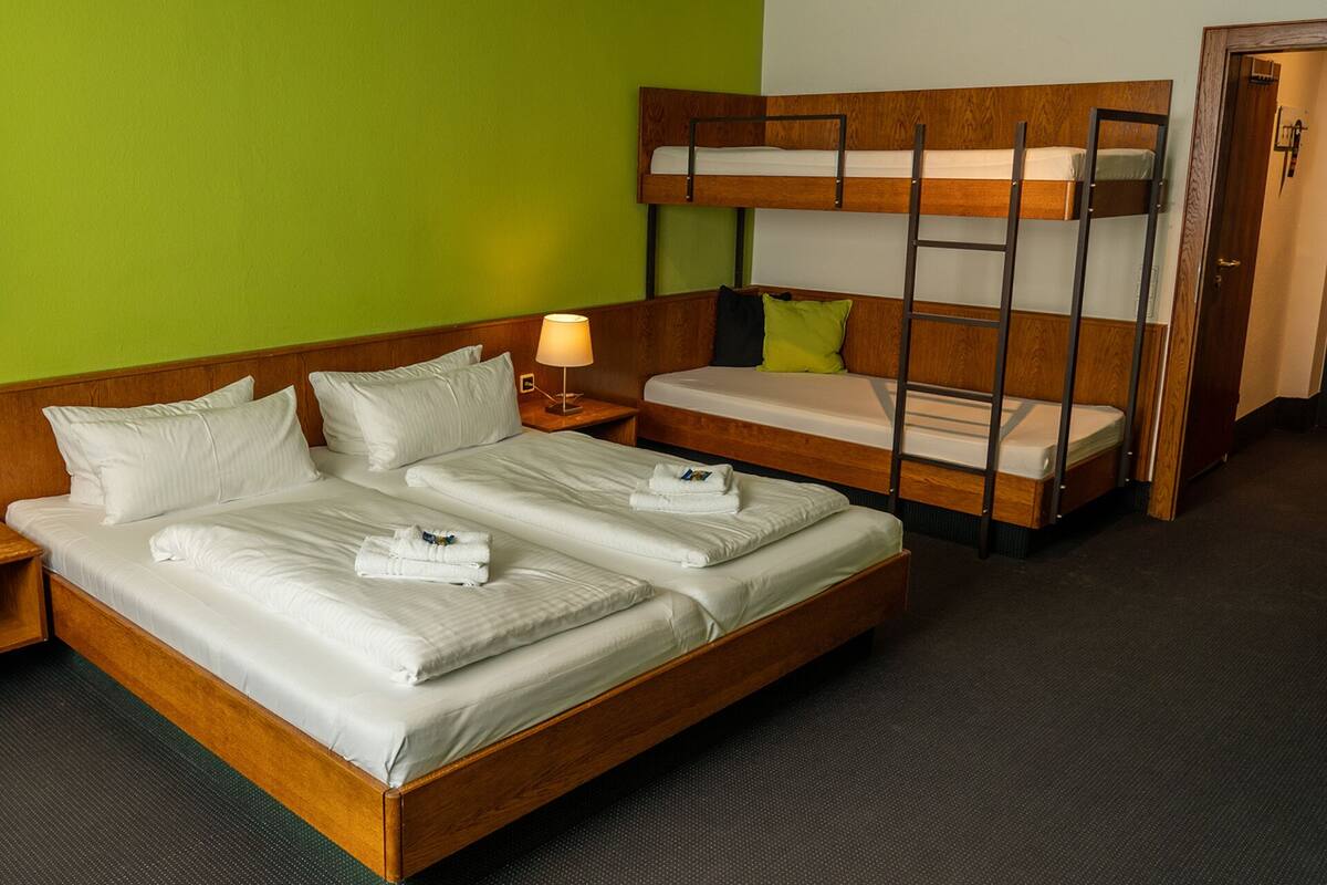 A hotel room with a wooden bed, a bunk bed, and a nightstand with a lamp.