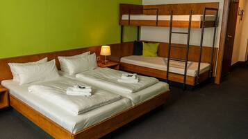 A hotel room with a wooden bed, a bunk bed, and a nightstand with a lamp.