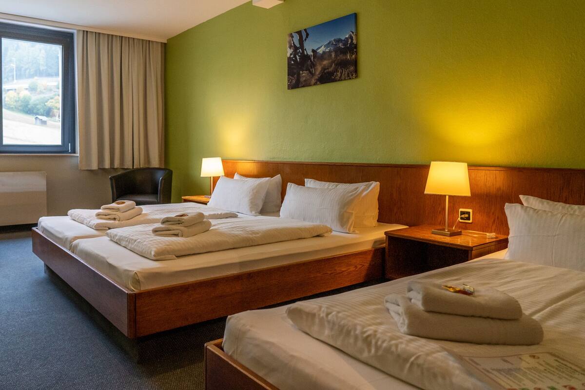 A hotel room with two beds, a large window, and a painting on the wall.