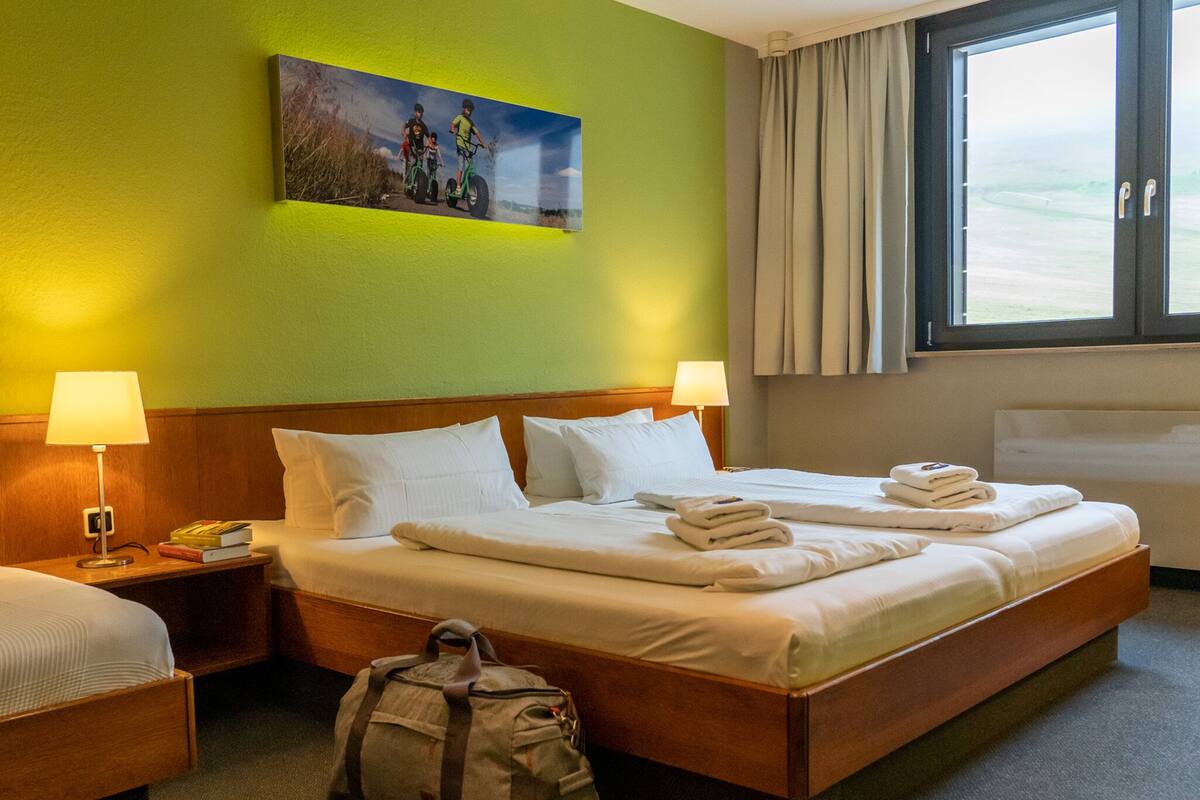 A hotel room with a large bed, two bedside tables, a lamp, a painting, and a window with curtains.