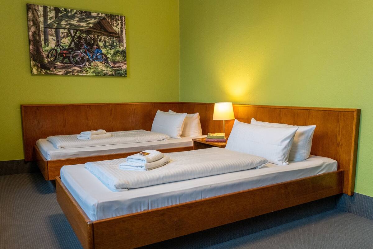 A hotel room with two single beds, a wooden headboard, a nightstand with a lamp, and a painting on the wall.