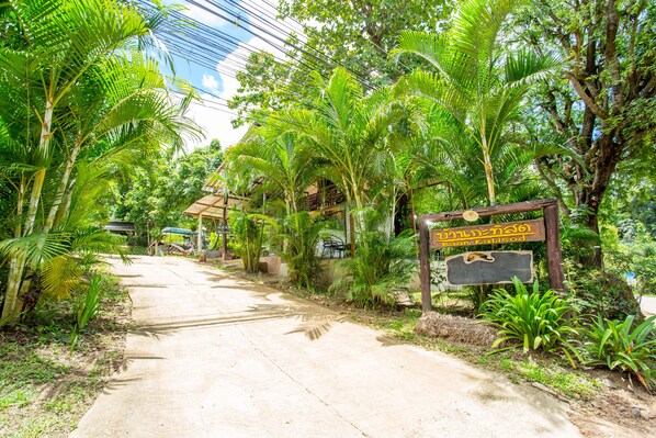 Un sendero pavimentado atraviesa un exuberante jardín tropical con palmeras y un letrero de madera.