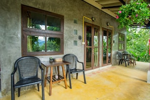 A covered patio with a table and chairs, a wooden door, and a view of greenery.